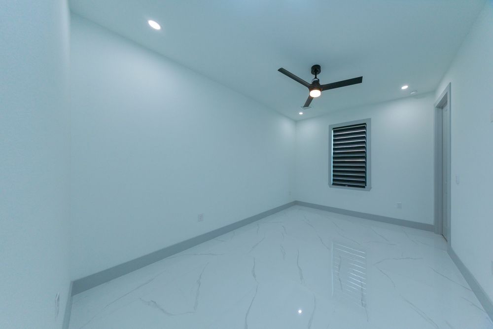 Bright empty bedroom with marble tile floors, ceiling fan, recessed lighting, and a small window.