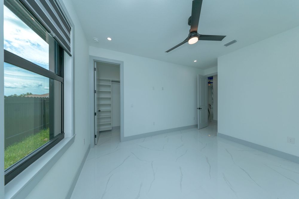 Spacious empty bedroom with large windows, ceiling fan, marble tile floors, and walk-in closet entrance.