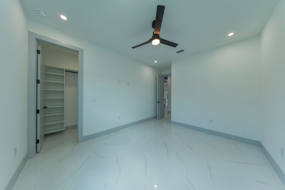 Clean modern bedroom with marble tile flooring, ceiling fan, recessed lighting, and open walk-in closet.