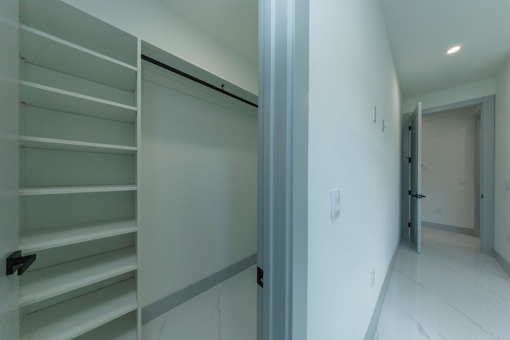 Bright walk-in closet with built-in shelving and hanging space leading to a hallway with marble floors.