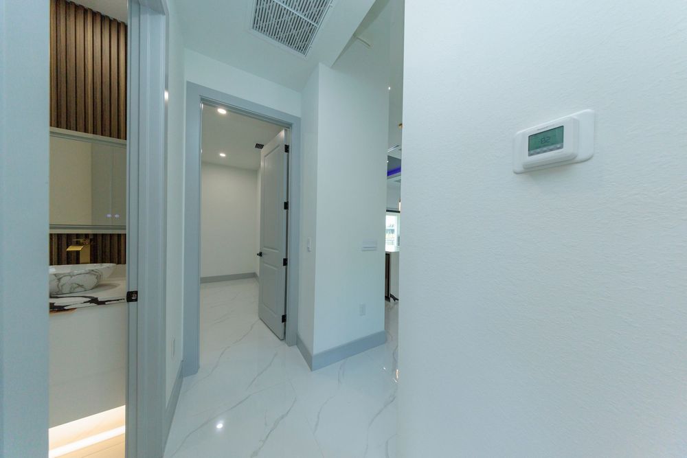 Modern hallway with marble tile floors, thermostat, recessed lighting, and view into adjacent bathroom.