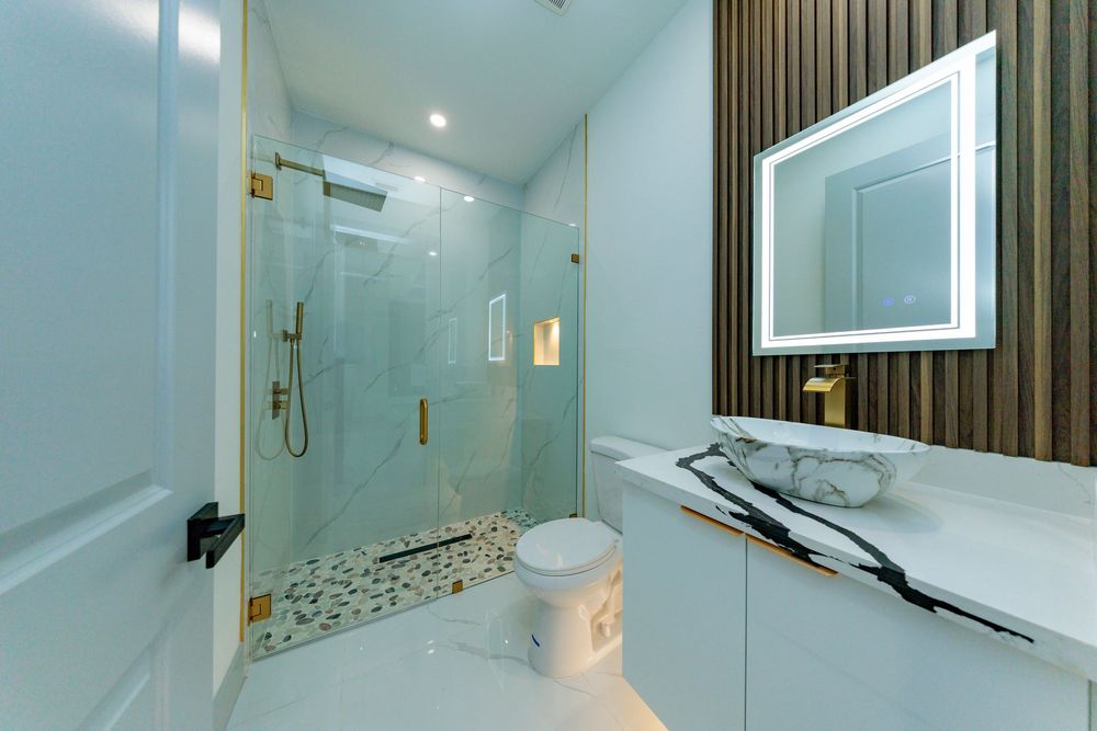 Elegant bathroom with glass walk-in shower, marble vanity, gold fixtures, LED mirror, and wood accent wall.