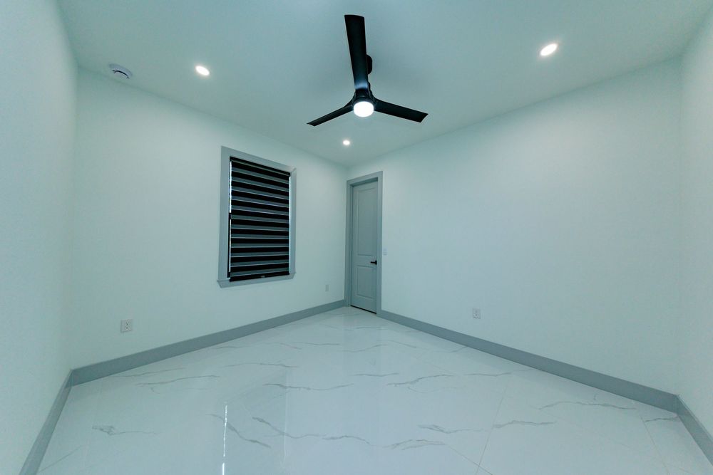 Minimalist empty bedroom with white marble tile floors, ceiling fan, recessed lighting, and a small window.