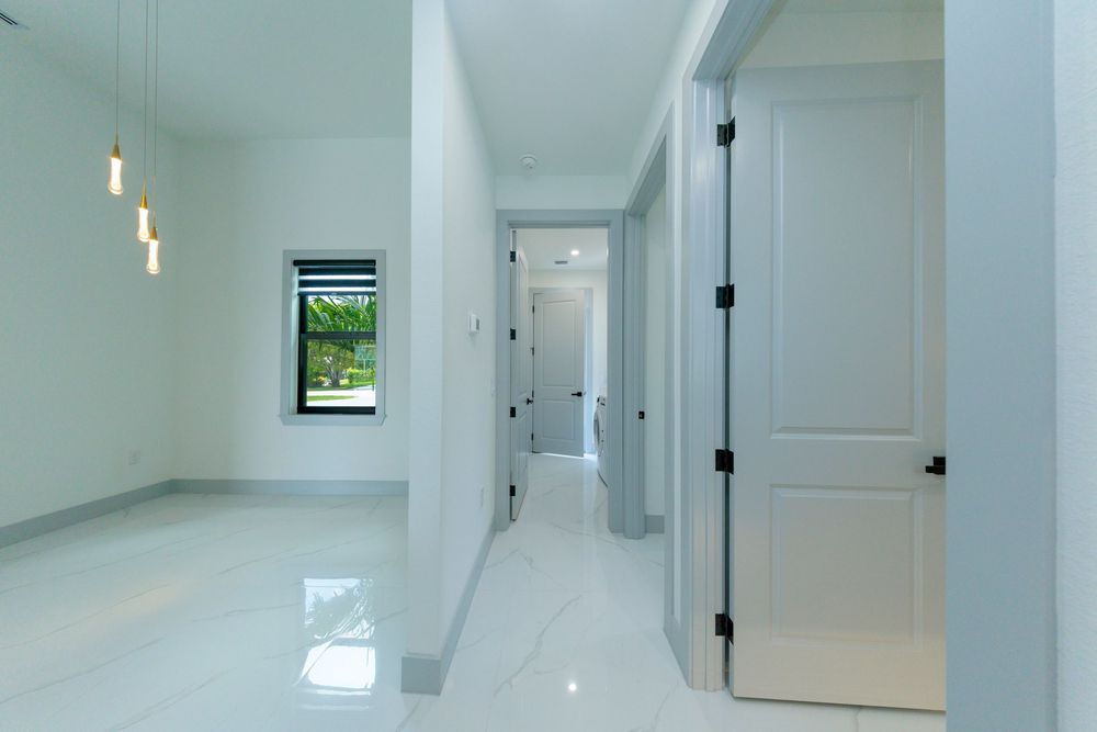 Bright modern hallway with glossy marble floors, white walls, pendant lights, and black door handles.