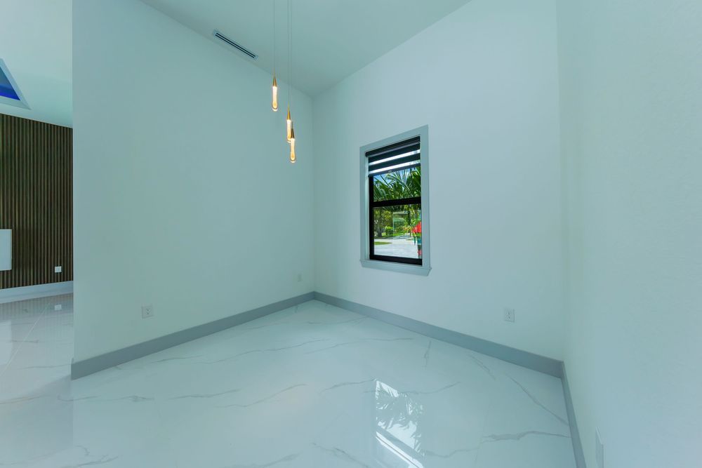 Minimalist empty room with marble tile flooring, white walls, pendant light, and a garden-view window.