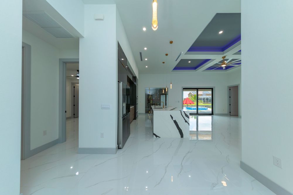 Expansive open-plan living space with marble floors, blue coffered ceiling, kitchen island, and pool view.