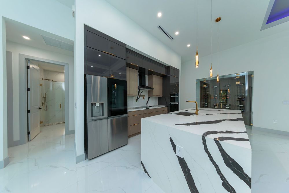 Modern kitchen with dramatic marble island, dark cabinetry, stainless steel refrigerator, and pendant lights.