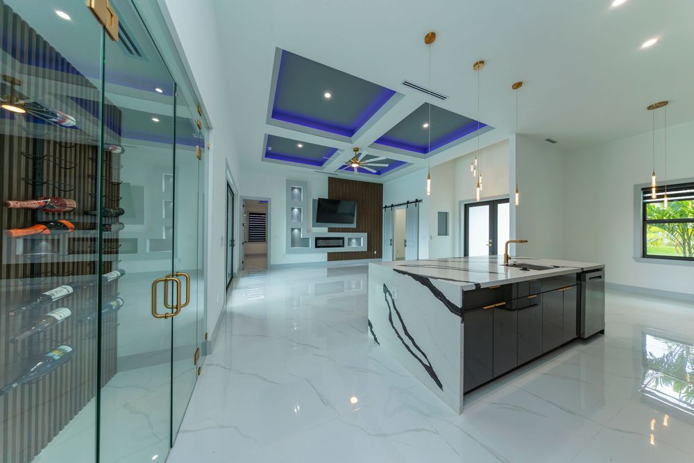 Luxury open-plan interior with marble floors, blue coffered ceiling, glass wine display, and kitchen island.