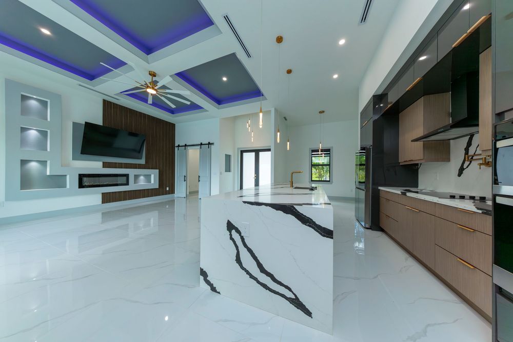 Modern open-plan kitchen with bold marble island, blue coffered ceiling, dark cabinetry, and ceiling fan.