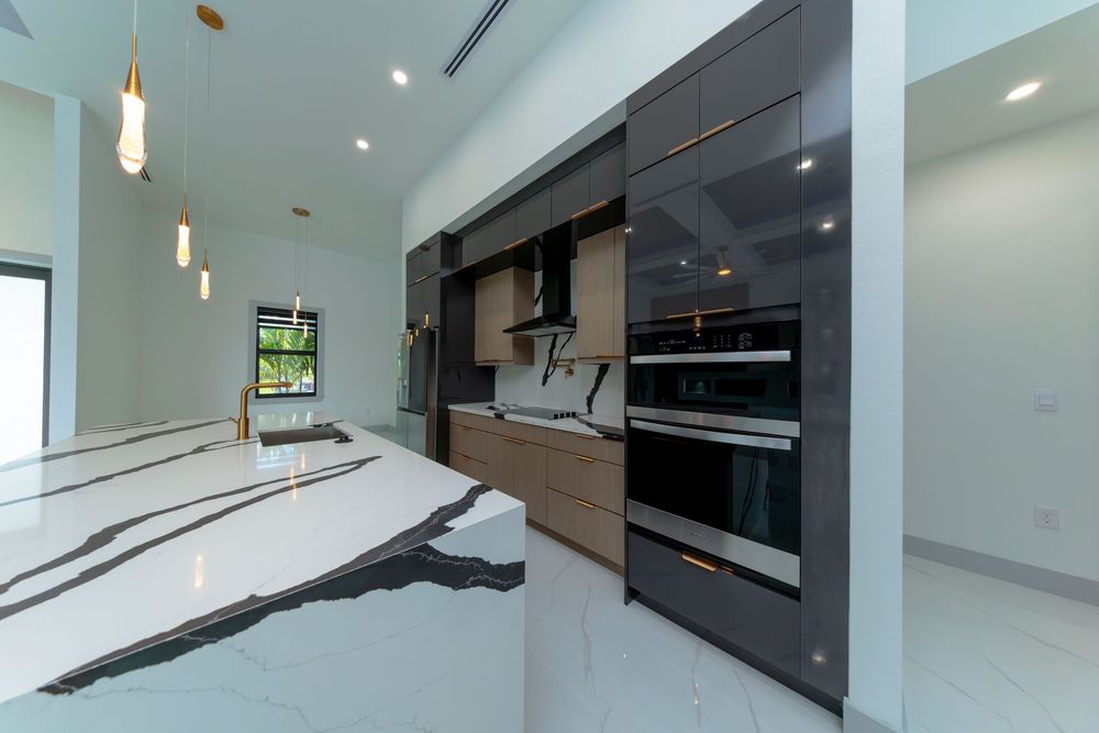 High-end kitchen with striking black and white marble island, dark gloss cabinets, and double wall ovens.