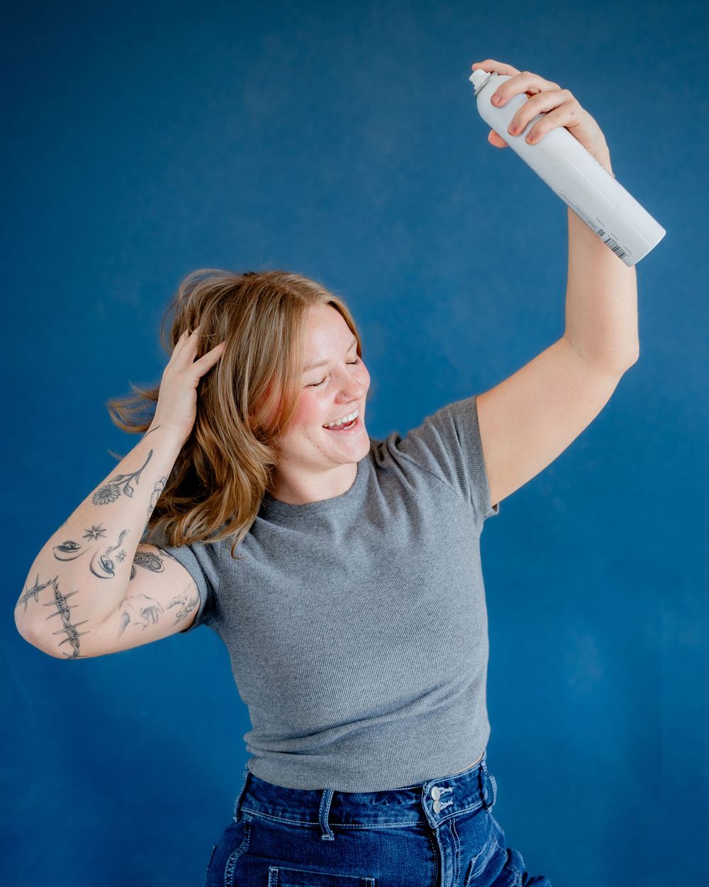 Woman in gray t-shirt and jeans poses joyfully against blue background in three-photo sequence.