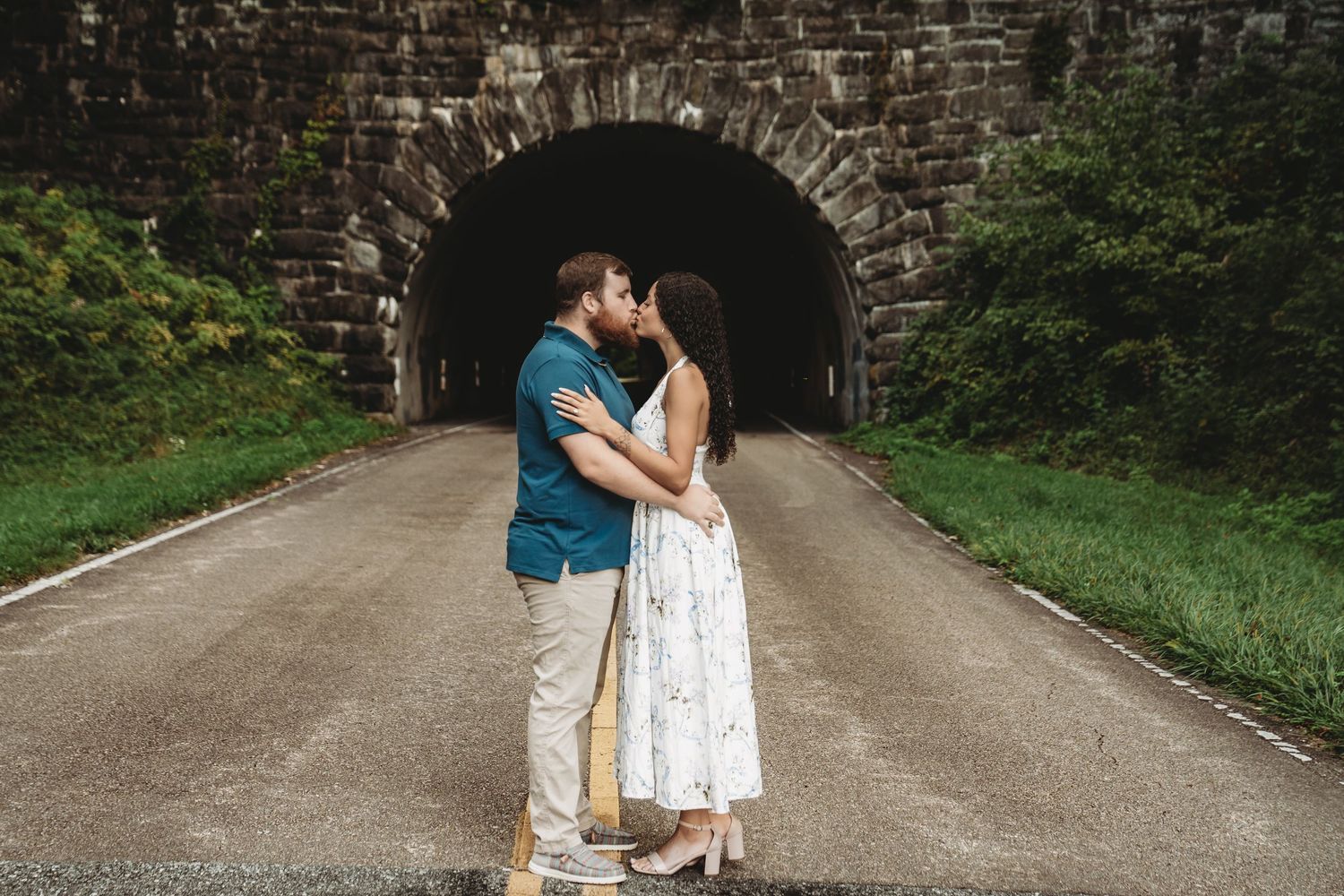 A couple embraces in front of a rustic stone bridge during their engagement session.