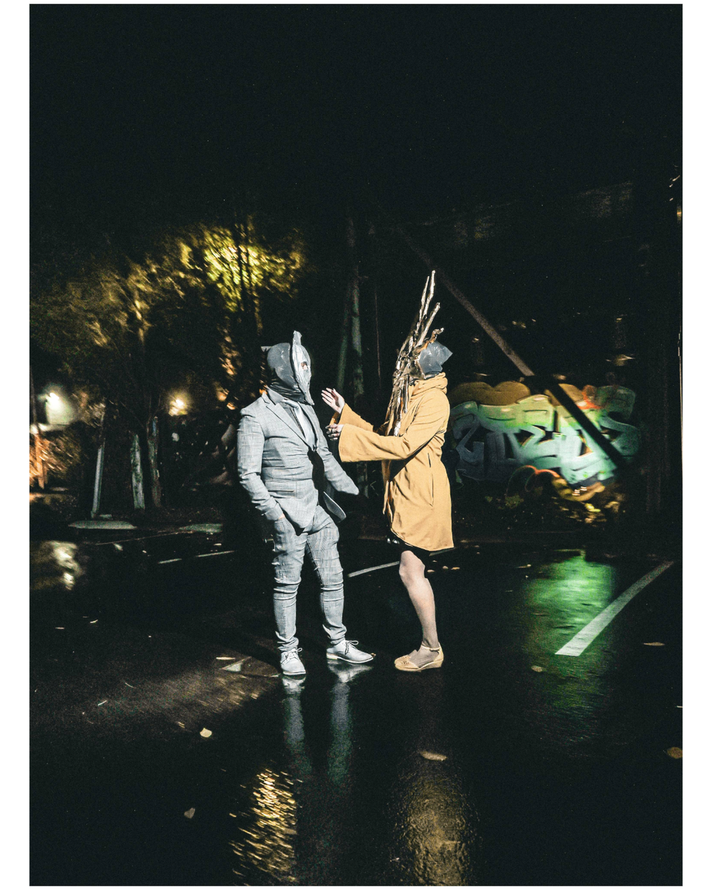 Two people in dark clothing sweep water on wet pavement at night with green lighting visible in the background.