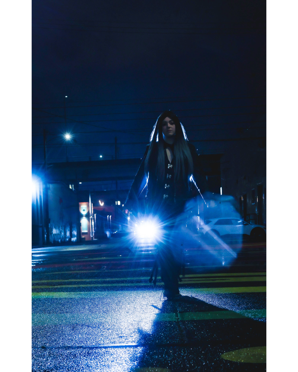 A silhouette dances in a moody blue-lit street at night with bright headlights and fog creating an atmospheric scene.