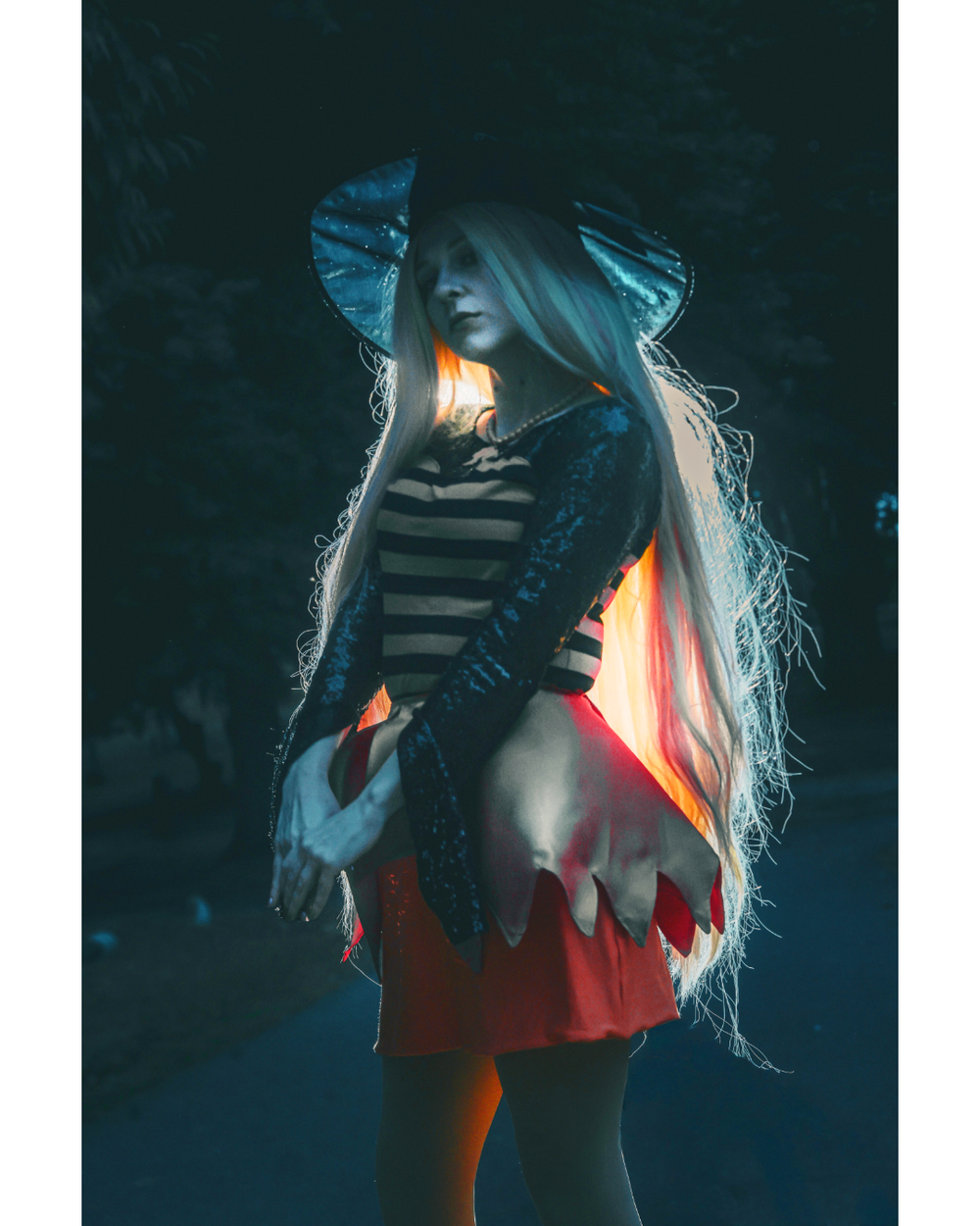 A figure in a dark setting illuminated by warm orange light creates a moody atmospheric portrait with long flowing hair.