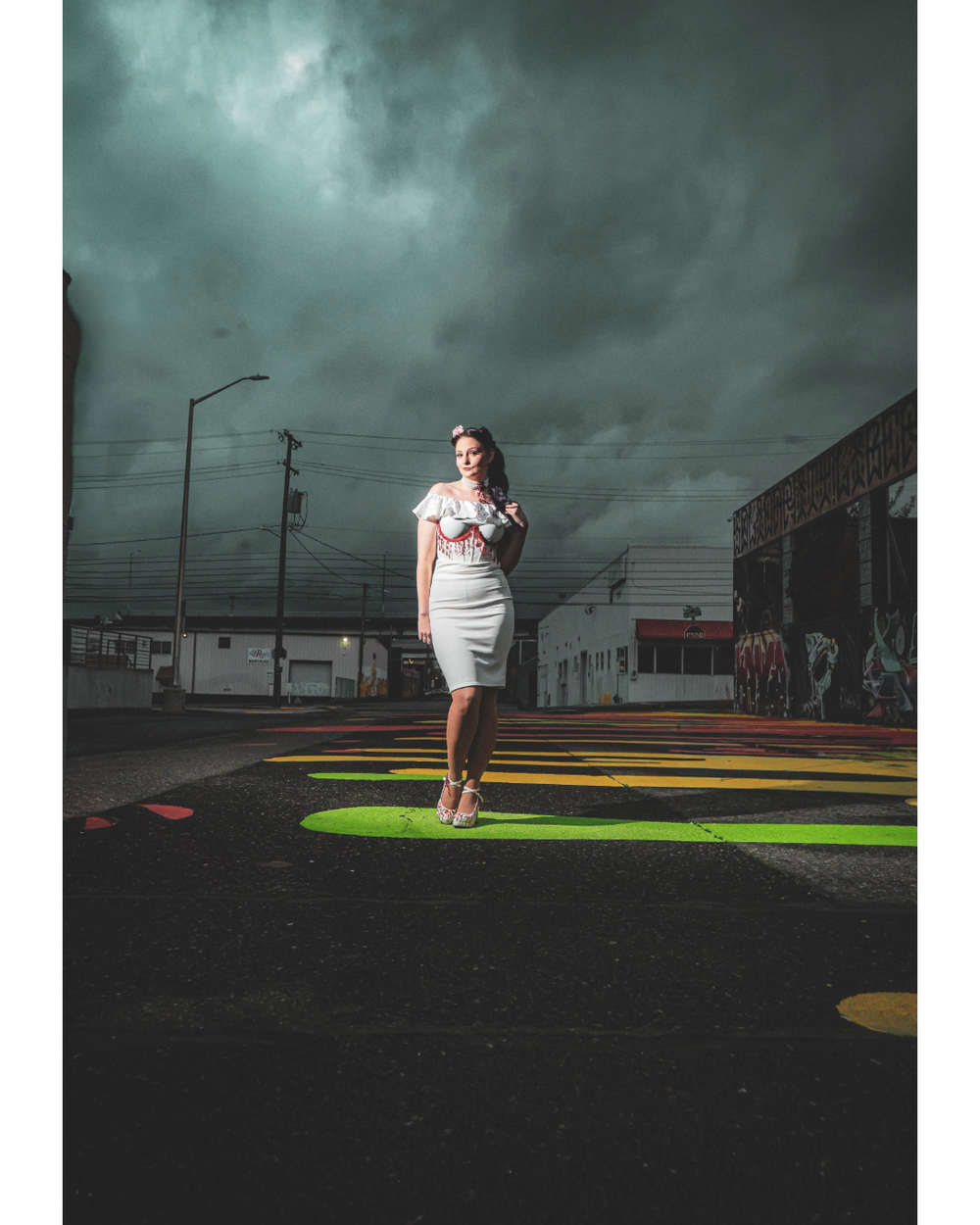A person in a white dress stands on a colorful painted surface under dramatic stormy skies.