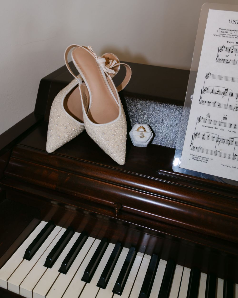 Wedding accessories including white heels and sheet music arranged on a wooden piano.