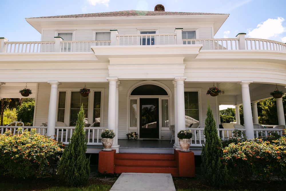 Elegant white mansion with columned porch and manicured landscaping serves as wedding venue.