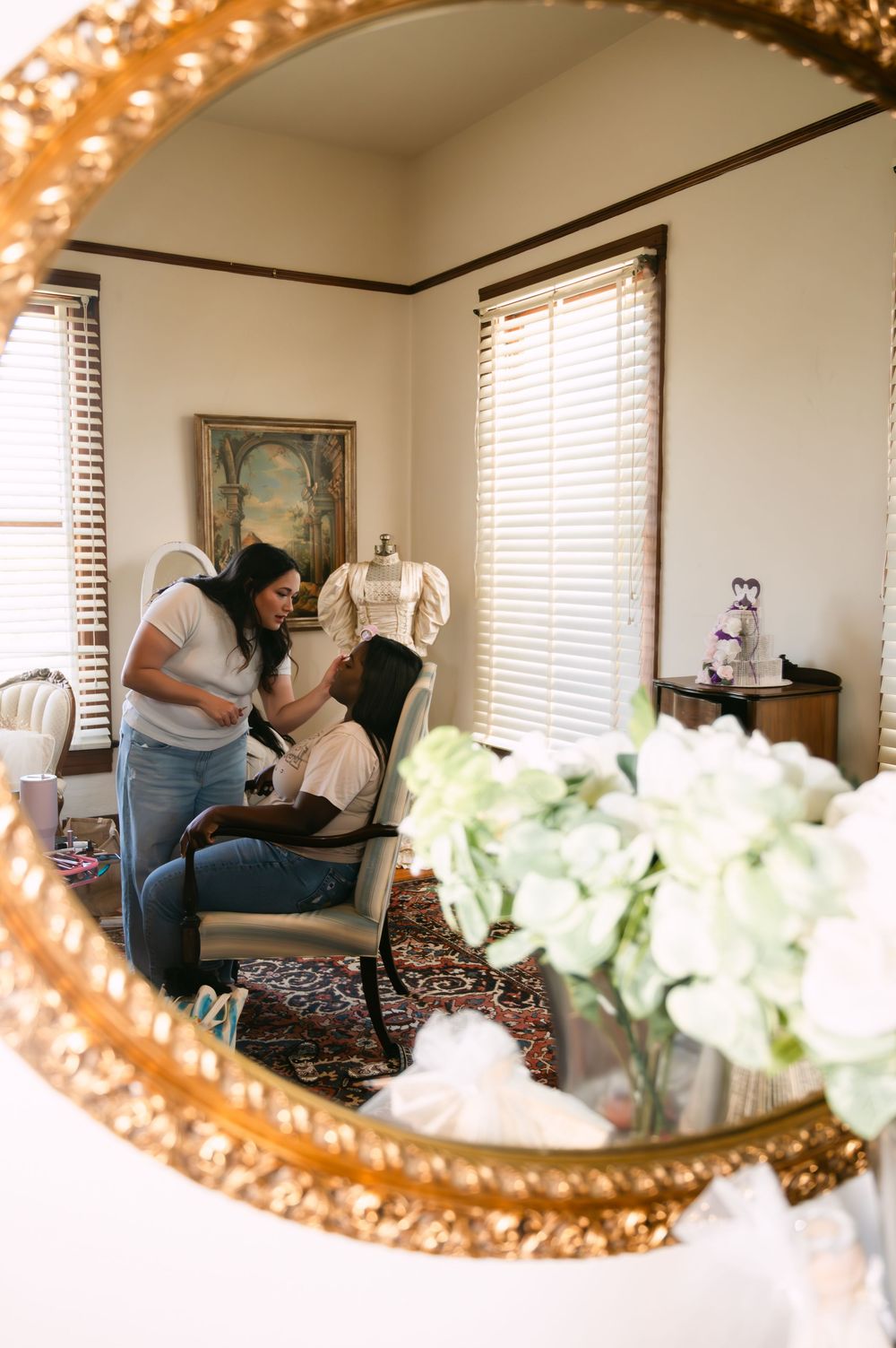 Reflections in an ornate gold mirror show wedding preparations in a sunlit room.