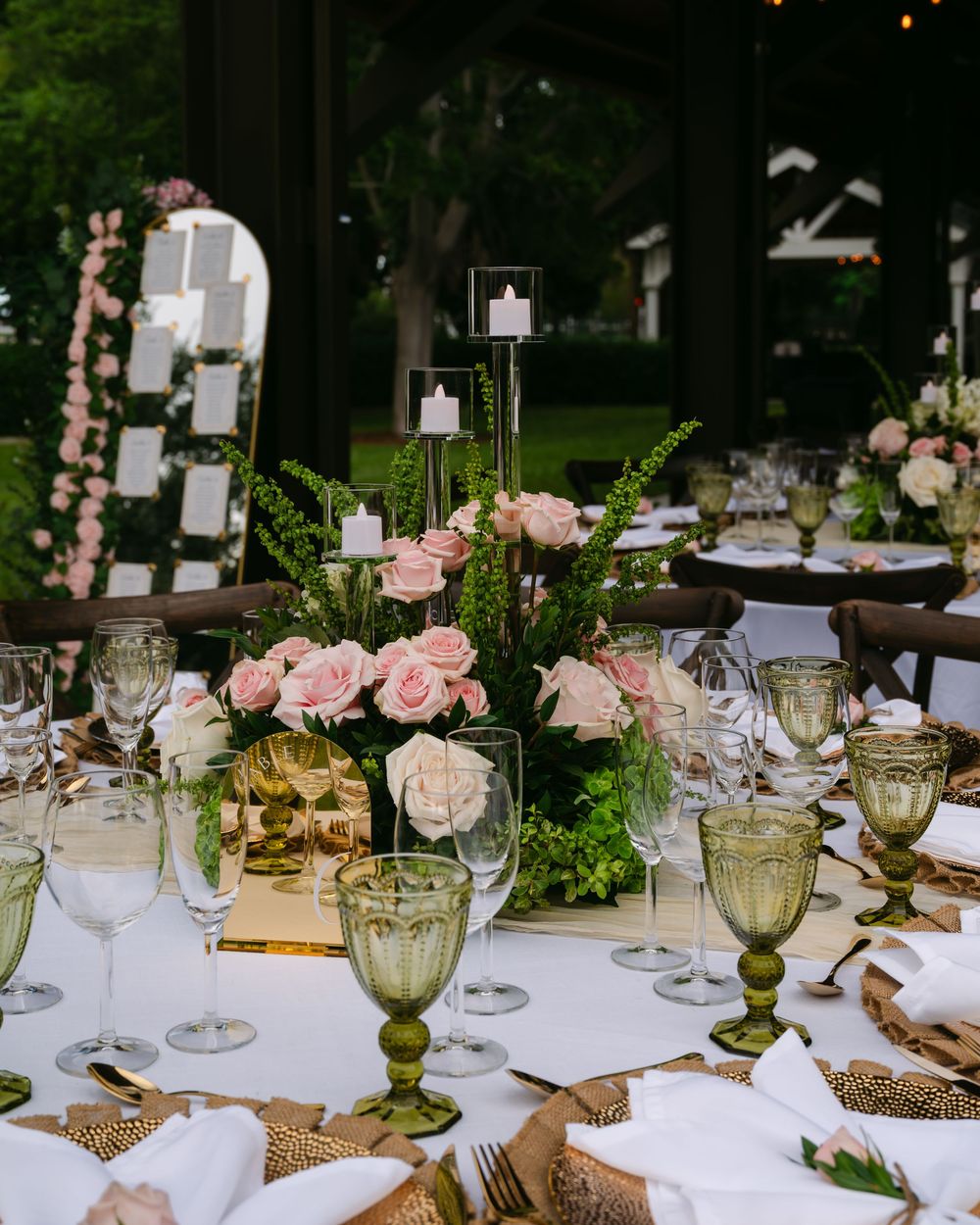Elegant wedding reception table setting with pink roses, green glassware, and white linens.
