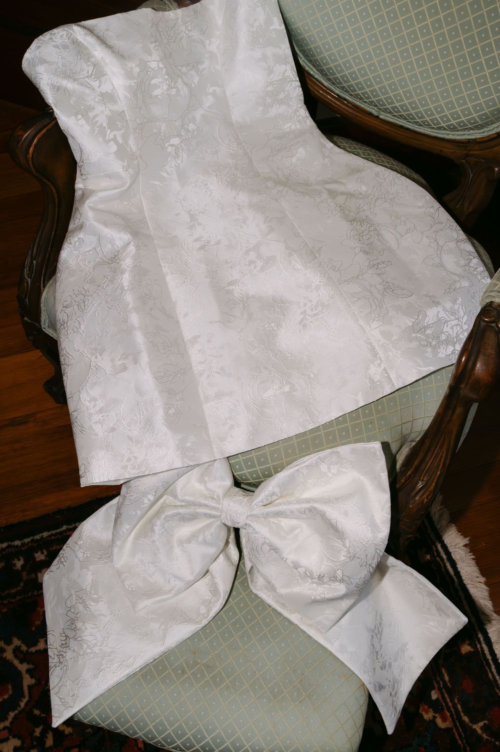 White wedding dress fabric with delicate lace patterns laid out on a green textured surface.