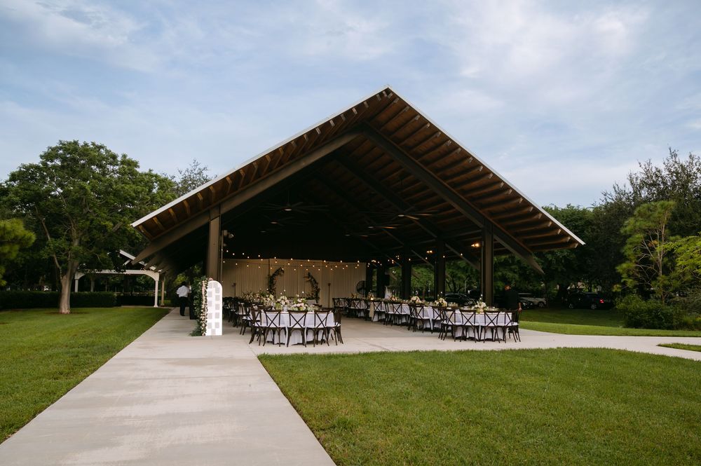Long covered outdoor pavilion with wooden beams and string lights set up for a rustic wedding ceremony.