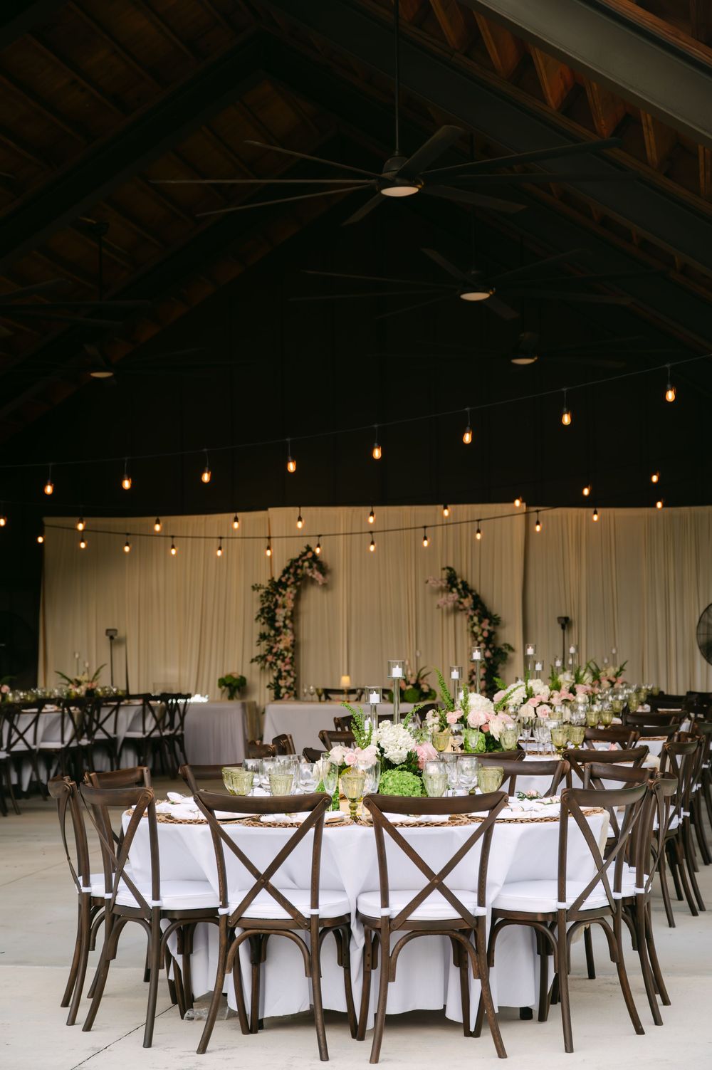 An elegant wedding reception venue with rustic wooden chairs and white tablecloths under string lights.