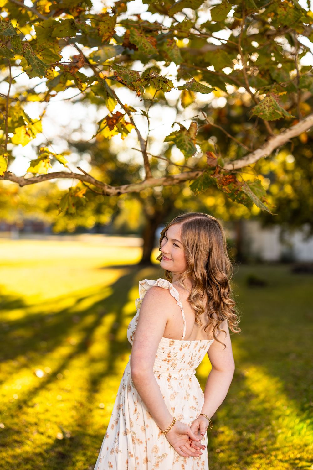 Floral dress portrait under autumn trees with golden sunlight filtering through leaves.