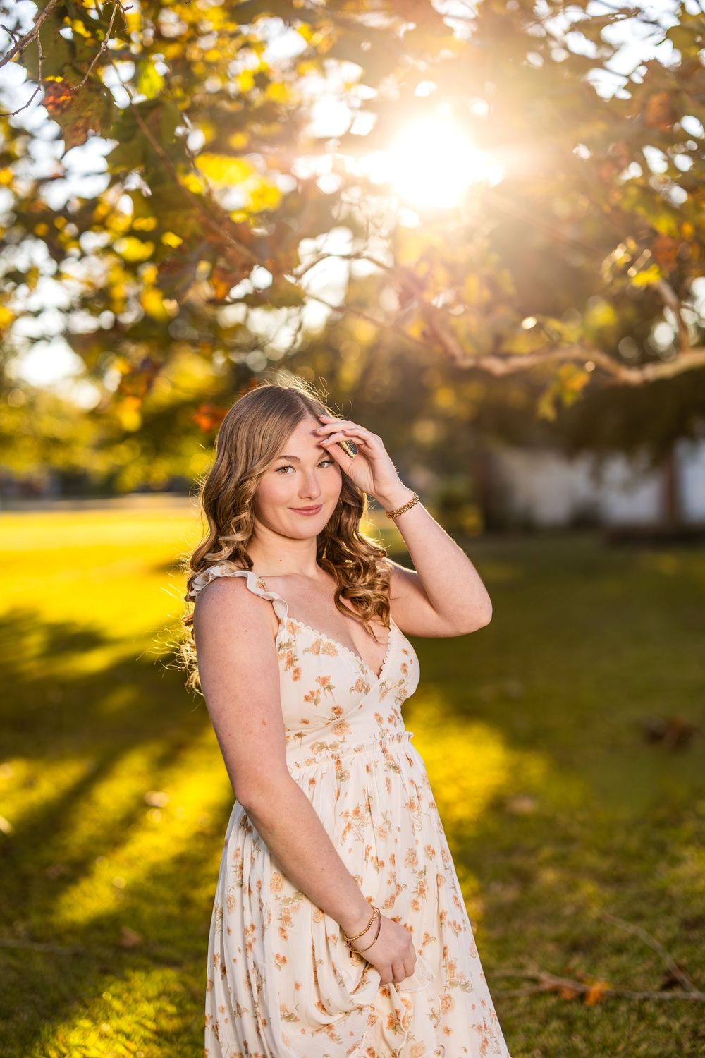 A floral sundress glows in golden autumn sunlight beneath trees with warm bokeh effects.