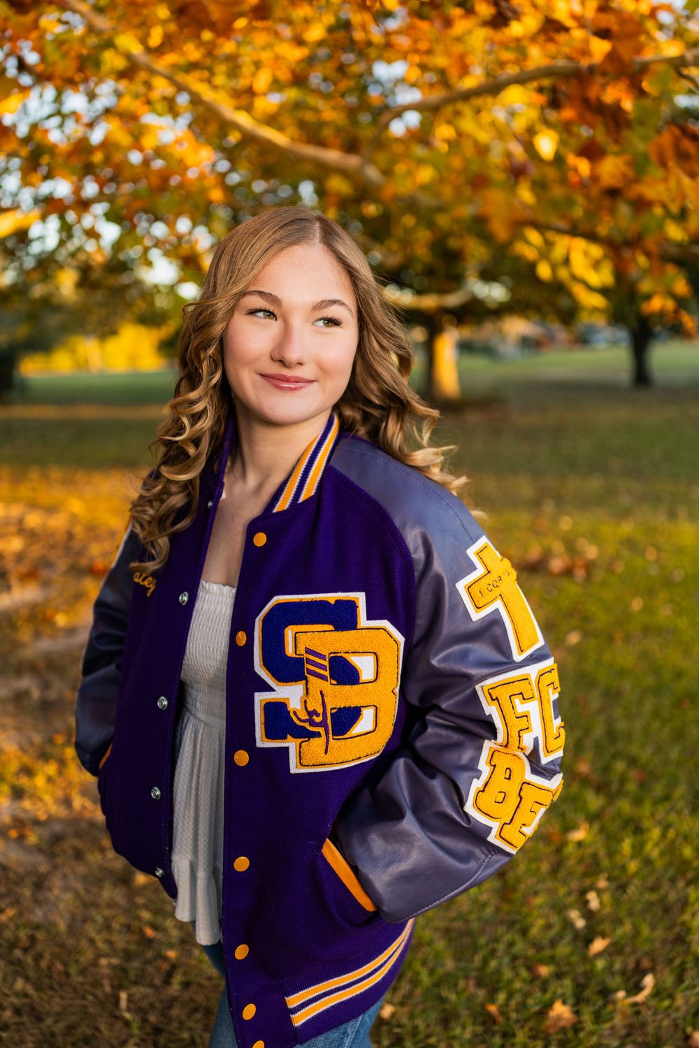 Navy blue varsity jacket with gold lettering shown in fall outdoor setting.