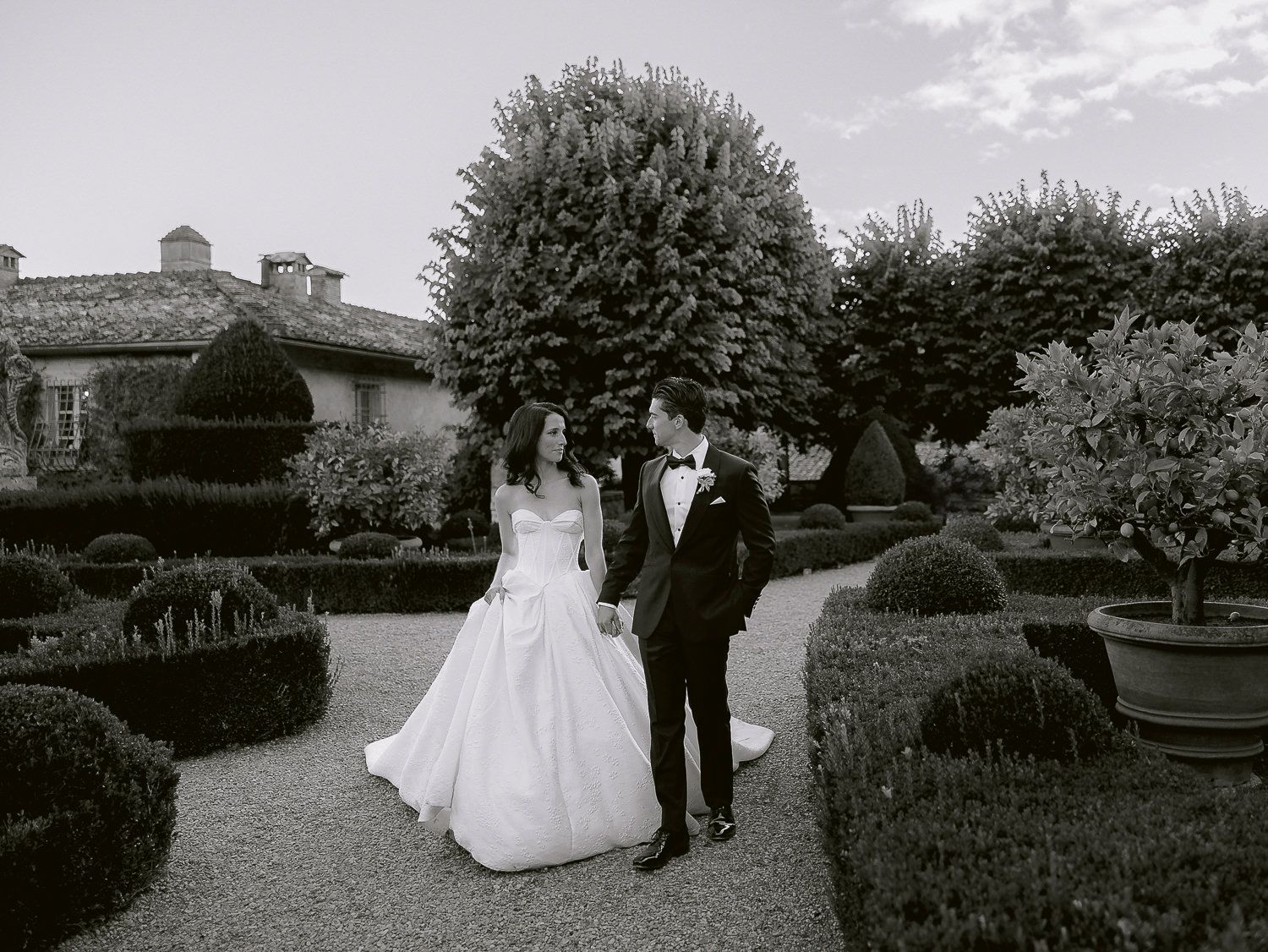 A black and white wedding photo collage showing couples in formal attire walking through a manicured garden setting.