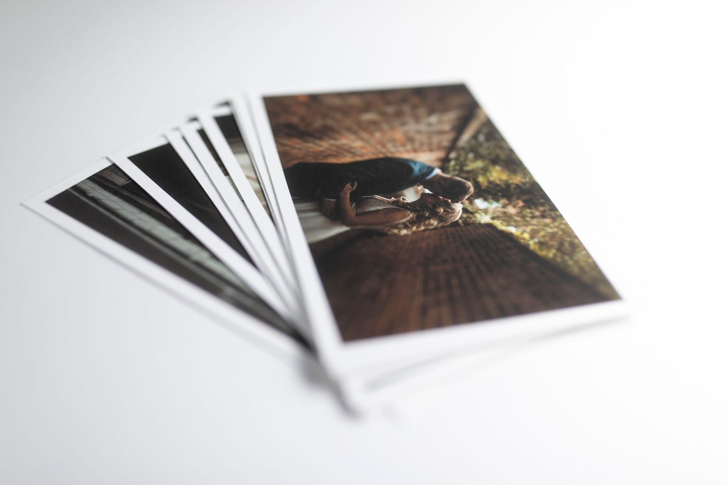 Stack of printed photographs fanned out on white surface showing artistic wedding detail shot.