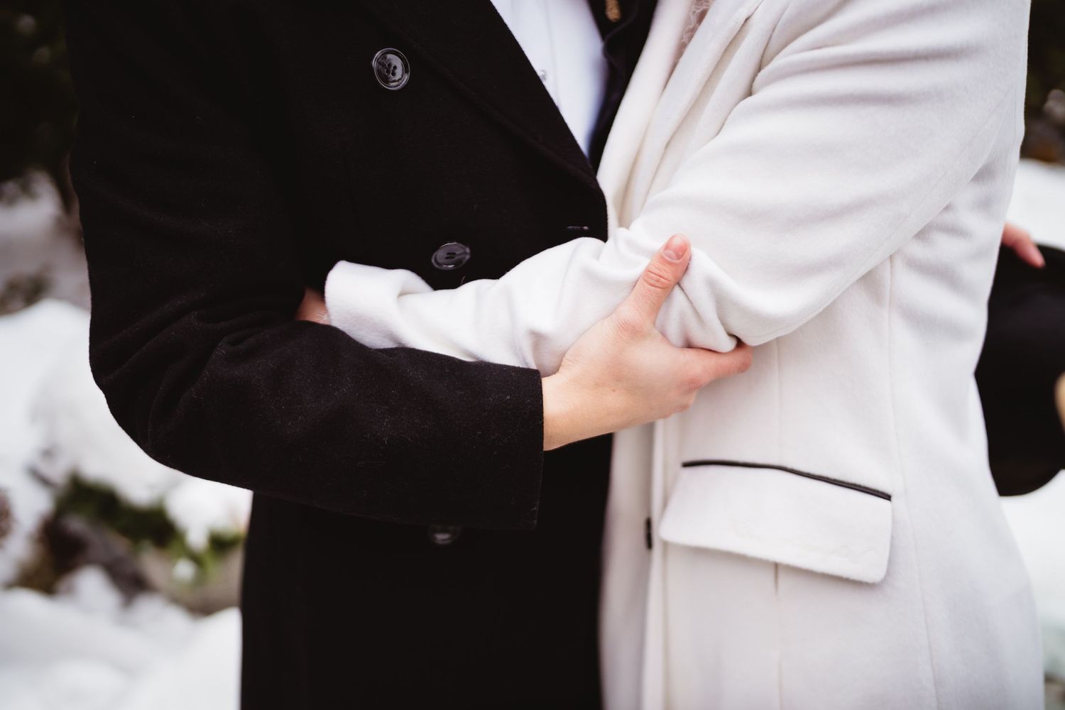 Close-up of two people in formal attire holding hands during a winter wedding ceremony.