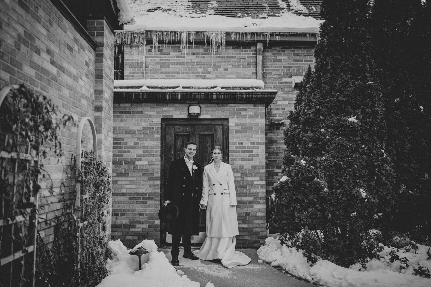 A couple stands in the doorway of a stone building during winter with snow on the ground.