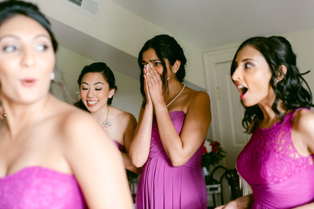Bridesmaids in magenta dresses react with excited expressions during wedding preparations.