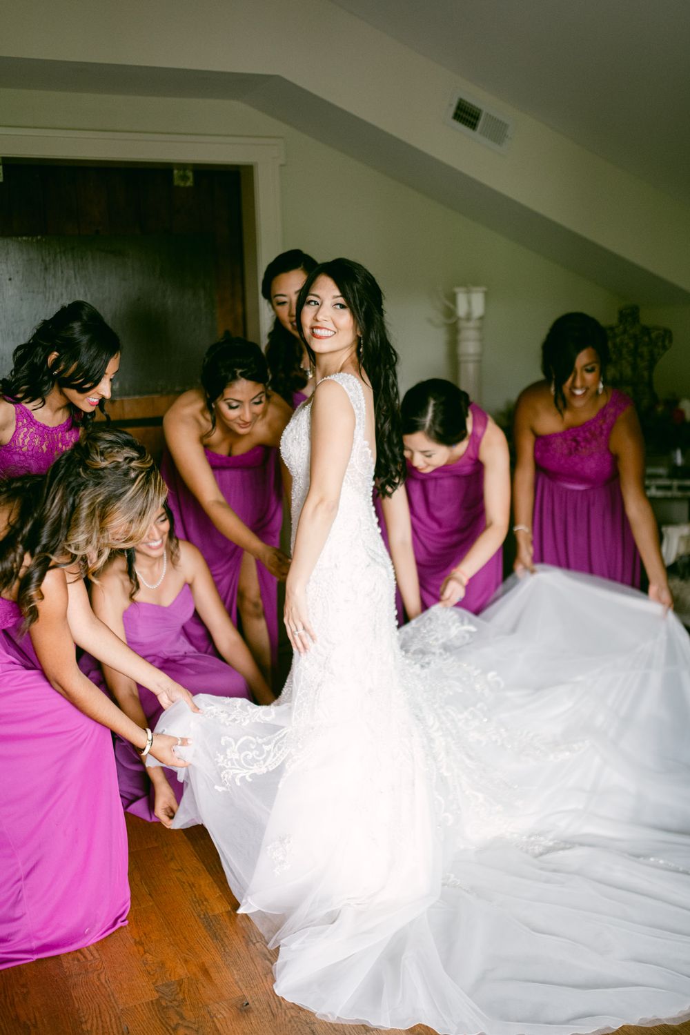 Bridesmaids in purple dresses gather around a bride in a white wedding gown during a pre-ceremony moment.
