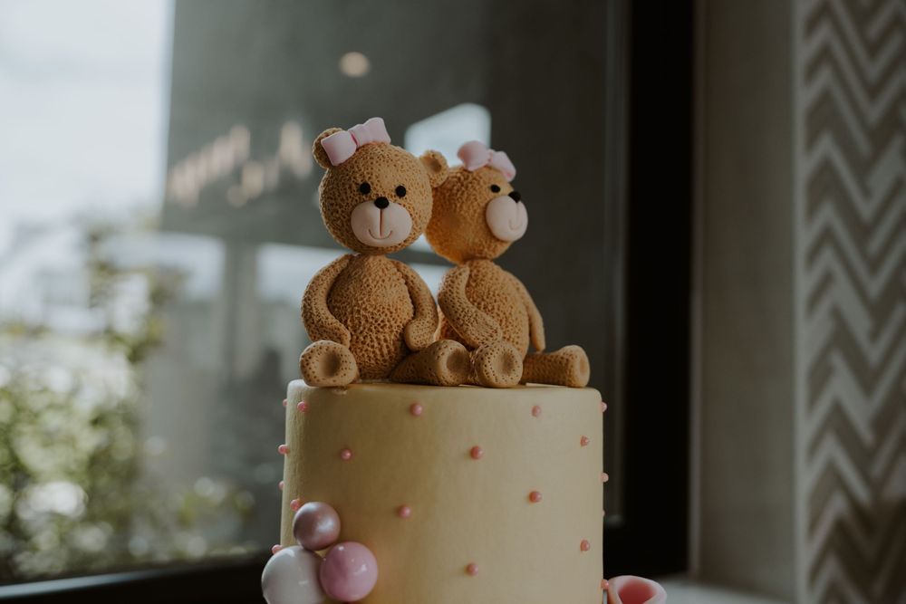 Wedding cake topper featuring two teddy bears with bows sitting on polka dot cake.