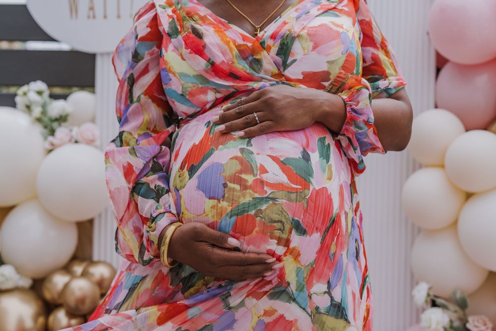 Person wearing floral maternity dress poses with balloon decorations.