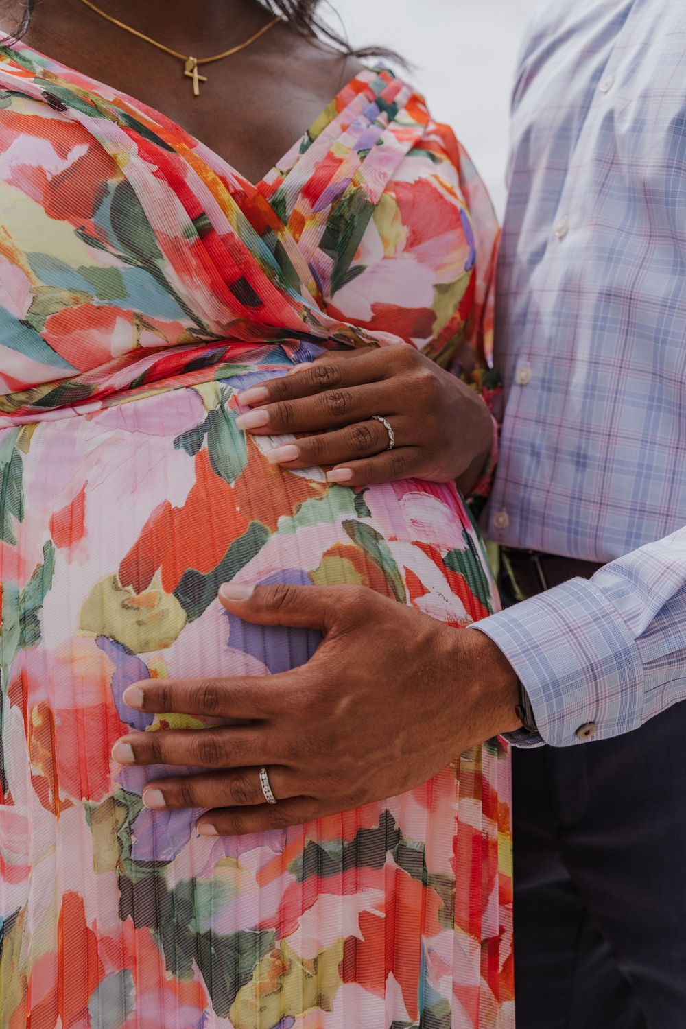 Close up of hands with wedding rings on pregnant belly in floral dress.
