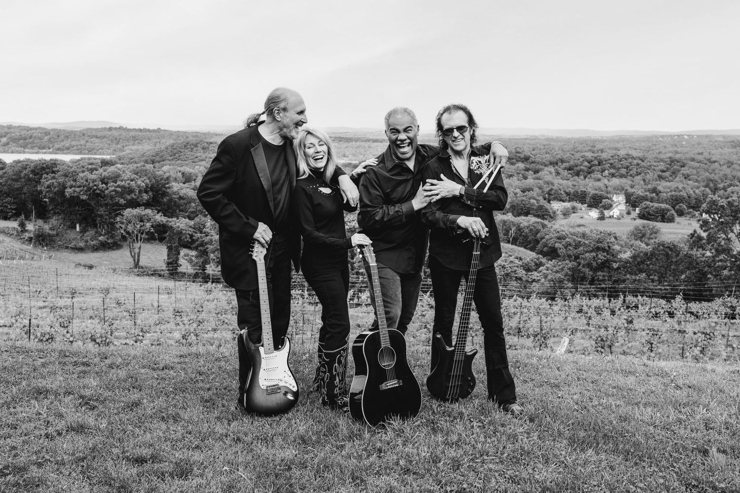 Group of friends standing together on hilltop overlooking scenic landscape in black and white photo.