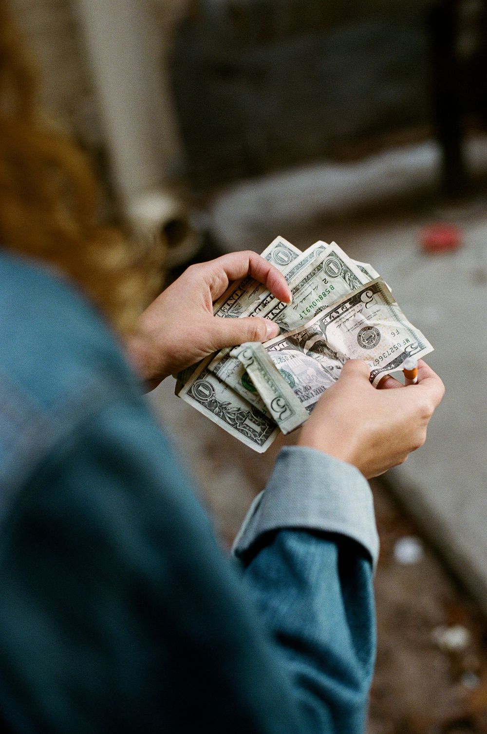 Hands counting dollar bills while wearing denim jacket.
