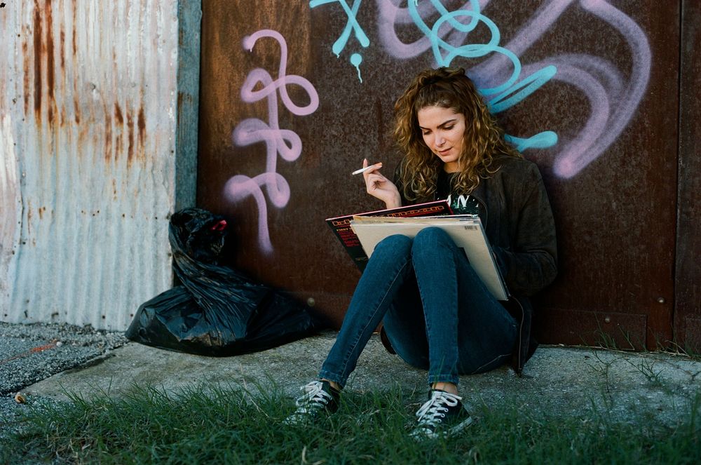 Person sitting against graffiti wall in denim jacket.