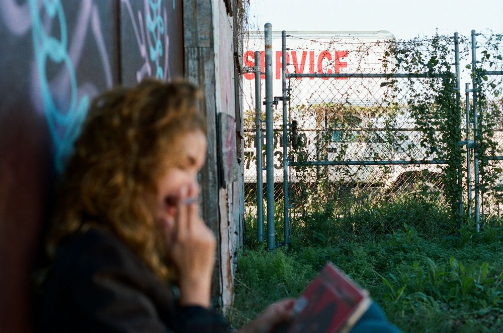 Person reading against graffiti wall with 'strange' text visible in urban setting.