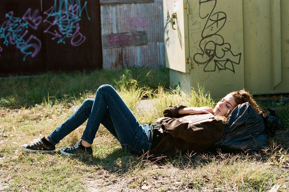 Figure lying on grass near graffiti wall in casual denim attire.