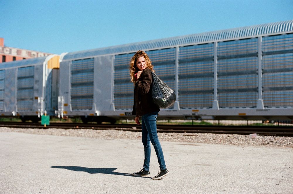 Figure in dark clothing standing near industrial building on sunny day.