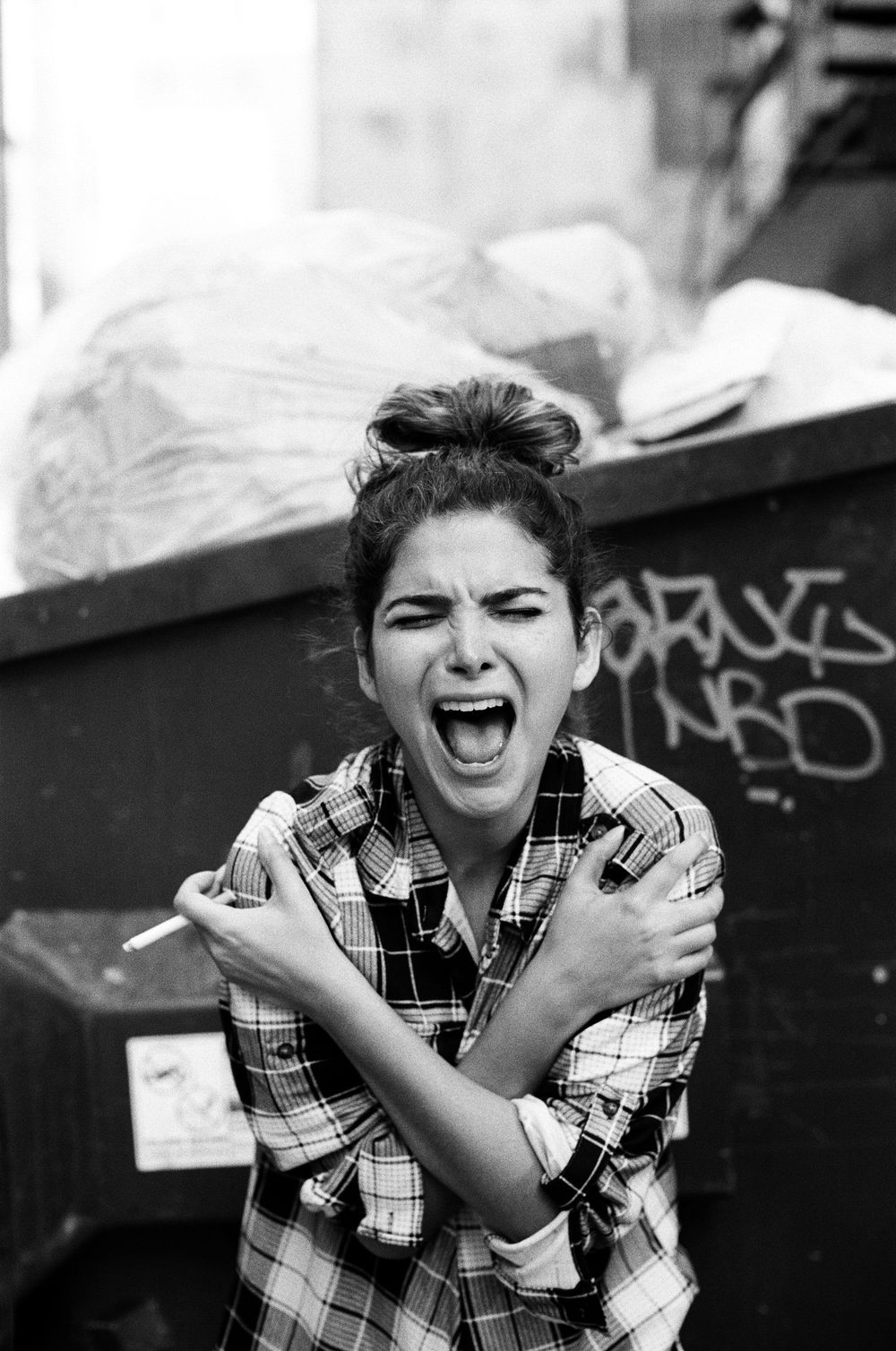 Person in plaid shirt expressing intense emotion against urban backdrop with graffiti.