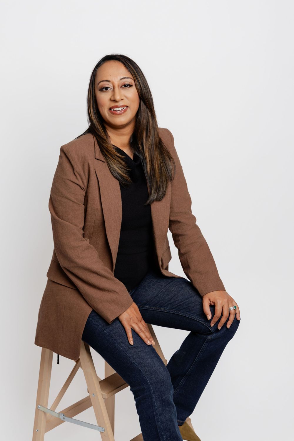 Professional portrait series showing a person in a brown blazer and dark jeans sitting casually on a wooden stool.