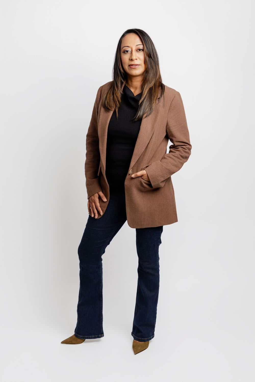 Full length studio portrait featuring brown blazer, black top and navy pants against white backdrop.