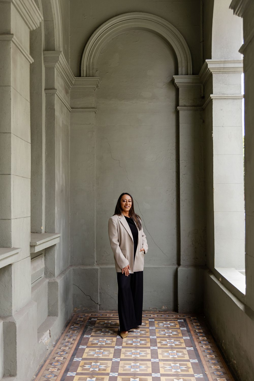 Person in dark clothing stands in an elegant arched corridor with patterned tile floor and white stone columns.