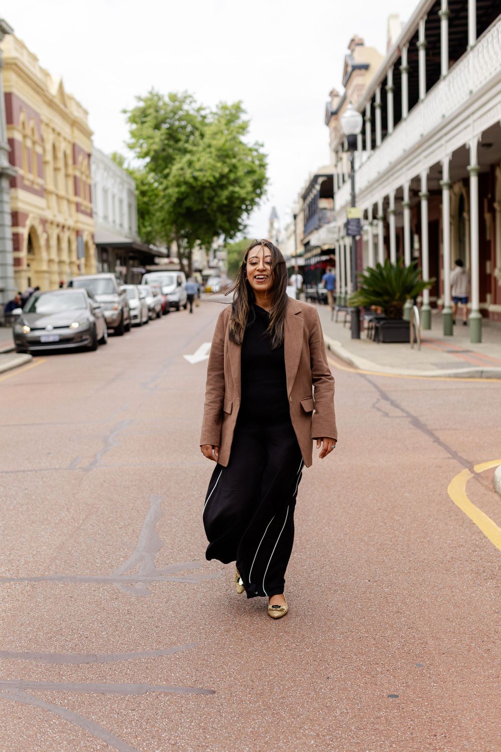 Street style photography showing a chic black dress and brown blazer ensemble in an urban setting.